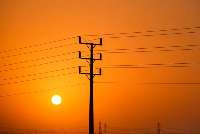 Silhouette of power lines at sunset against a vibrant orange sky.