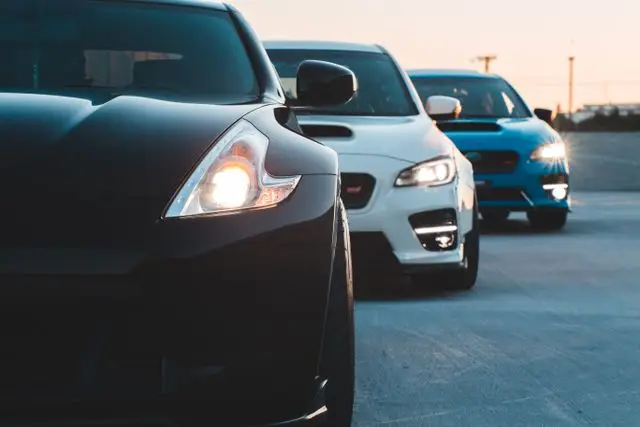 Contemporary sports cars with switched headlights parked in row on asphalt parking in twilight
