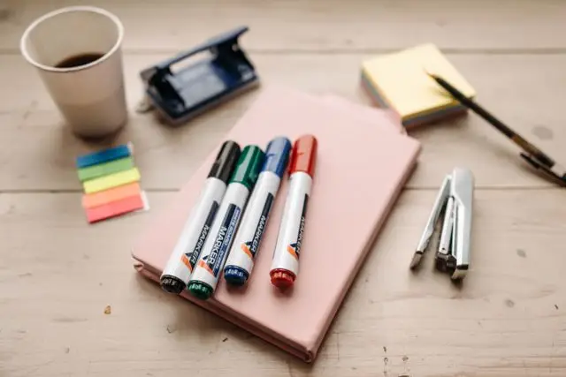 A flat lay of office supplies on a wooden table, including markers, sticky notes, and a coffee cup.
