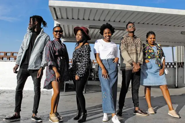 Stylish young adults in diverse fashion posing together on a rooftop under a sunny sky.